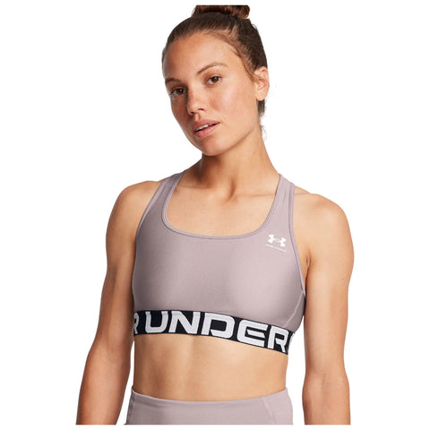 A woman is wearing a light purple athletic sports bra featuring a black band with the word "UNDER" prominently displayed. She is looking directly at the viewer with a neutral expression.