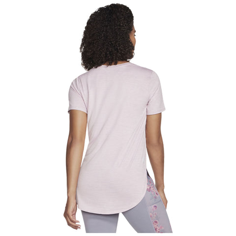 A person stands with their back facing the viewer wearing a light pink short-sleeve shirt and gray leggings with floral designs on the side. The environment is neutral and unobtrusive.