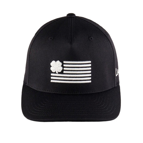 A black cap is displayed featuring an embroidered design of a four-leaf clover next to horizontal stripes resembling a flag with white stitching. The cap has a curved brim.