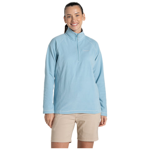 A woman stands smiling, wearing a light blue fleece pullover with a zip collar and beige shorts in a neutral background, creating a casual, outdoor attire appearance.