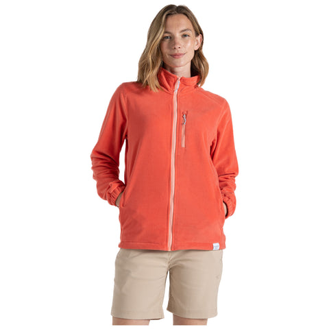 A woman stands confidently in an orange fleece jacket with a zippered pocket smiling while wearing light beige shorts in a simple background.