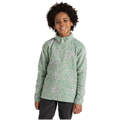 A young child is smiling while wearing a light green fleece jacket with pink floral patterns. The child stands against a plain white background, exuding a cheerful demeanor.