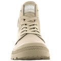 A beige high-top shoe with multiple eyelets and laces is positioned upright facing forward in a neutral setting featuring a textured rubber sole and branded label on the tongue.