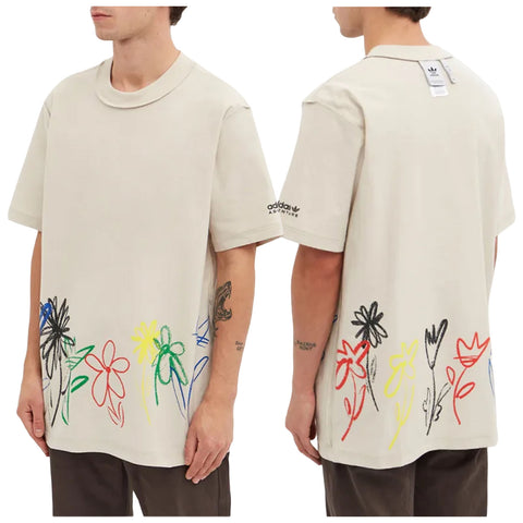 A light beige oversized t-shirt features colorful flower designs along the bottom. A person wearing the shirt stands with arms relaxed in a neutral background, showcasing the casual style.