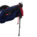 A blue and red backpack with a support stand is positioned upright showcasing multiple compartments and straps designed for outdoor or travel activities providing easy access to its contents.