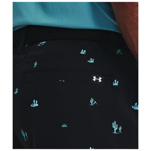 Black shorts adorned with light blue cactus and sun patterns are positioned at the forefront with a small brand tag visible at the back pocket against a solid color background.