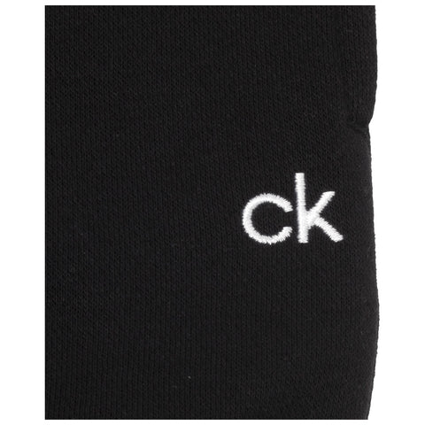 A black sock sits prominently with the letters "ck" embroidered in white on its side, highlighting a simple yet recognizable brand design in a plain background.