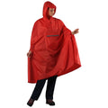 A woman is wearing a large red rain poncho with a hood while standing and holding the fabric. She is dressed in dark pants and is on a plain background.