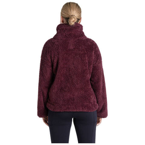 A person wearing a burgundy fluffy jacket stands with their back to the viewer, in a neutral setting that emphasizes the cozy texture of the garment.