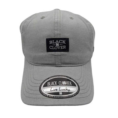 A gray baseball cap features a black patch labeled BLACK CLOVER and a circular sticker that reads BLACK CLOVER Live Lucky on the brim against a plain white background.