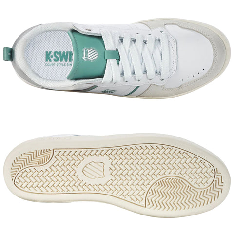 A white sneaker with green accents sits flat, showcasing its laces and logo on the tongue. The sole features a textured pattern suitable for grip and traction.