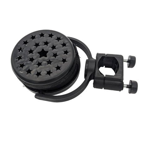 A circular black device with a star-patterned surface rolls up while being held by a mounting clip suggesting use for organizing or securing cables in a workspace or similar environment.