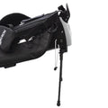 A black golf bag features compartments for clubs and accessories while a sturdy stand supports it upright on the ground allowing easy access in a golf course setting.