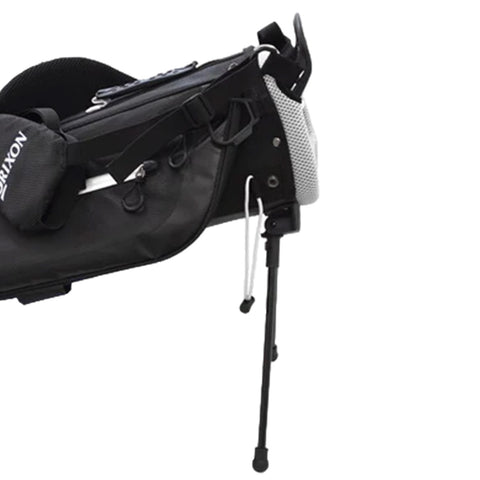 A black golf bag features compartments for clubs and accessories while a sturdy stand supports it upright on the ground allowing easy access in a golf course setting.