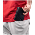 A person wearing a red shirt and gray shorts stands with a black wallet partially tucked into their back pocket while their hand gestures suggestively behind the wallet.