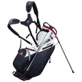 A golf bag with shoulder straps stands upright on a small tripod. Its design features a combination of white and black colors with red accents, intended for easy transport on the golf course.