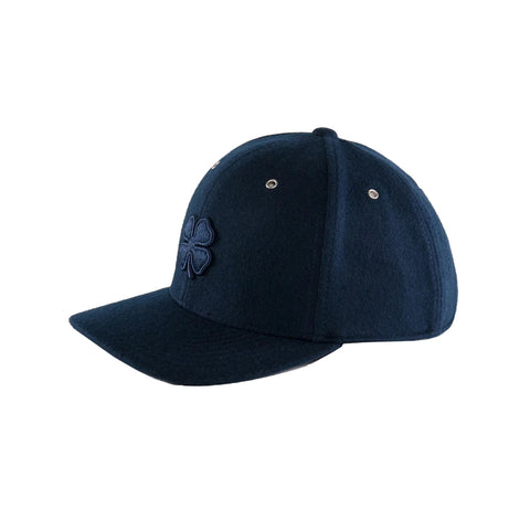 A navy blue cap with a stitched four-leaf clover emblem rests on a flat surface showcasing its structured shape and solid color in a minimalistic setting.