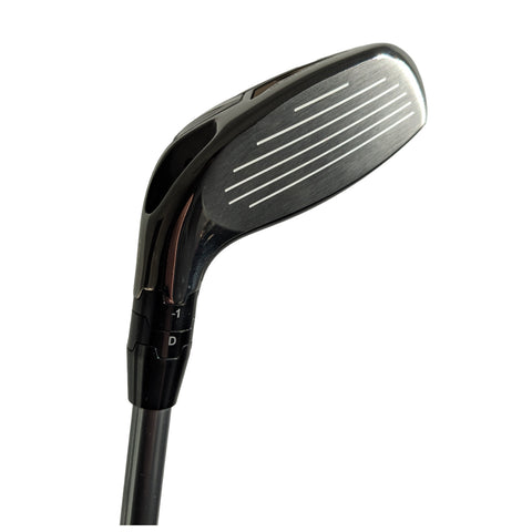 A golf club head is shown positioned at an angle with a shiny metal surface and alignment grooves indicating precision. The club is part of golf equipment used for playing on grassy courses.