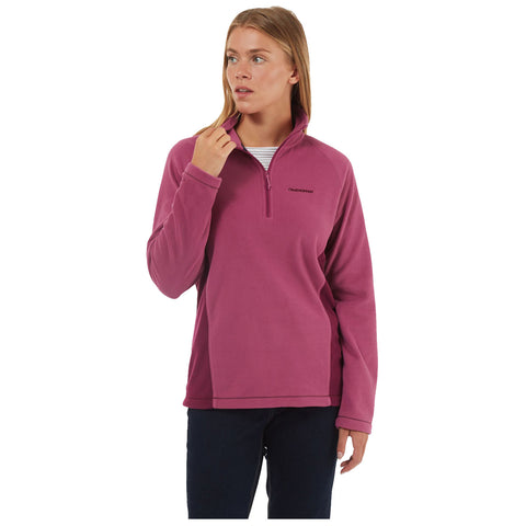 A person wears a pink fleece pullover, partially unzipped, while looking thoughtfully away. The setting is neutral, emphasizing the clothing and the individual’s contemplative pose.