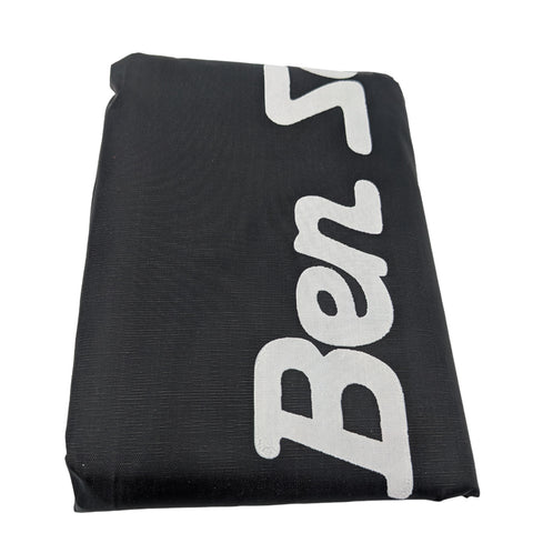 A black rectangular object with a white stylized text "Ben S" prominently displayed is lying flat. The surface has a textured appearance suggesting a fabric material.