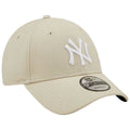 A beige baseball cap with a white embroidered logo prominently featuring the letters NY rests on a flat surface highlighting its structured peak and mesh-like texture in a minimalist setting.