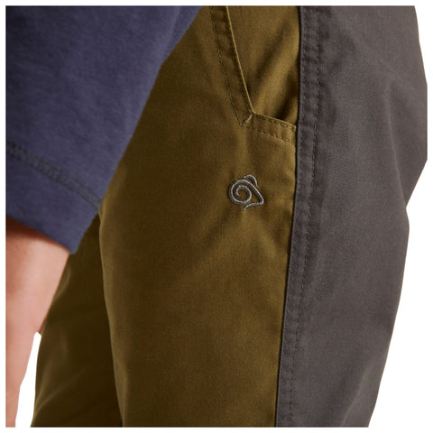 A close-up of olive and dark gray pants with an embroidered spiral logo on the pocket and part of a navy sleeve visible in the background.