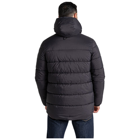 A person is wearing a black puffer jacket with a hood standing with their back to the viewer in a neutral setting showcasing the jacket's quilted design and relaxed fit.