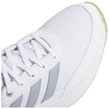 A white sneaker with a textured surface and gray stripes is positioned prominently with laces threaded through eyelets while casting a light shadow on a plain background.