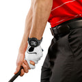 A hand grips a golf club wearing a white glove while displaying a smartwatch with data. The person is dressed in a red shirt and black pants with a belt.