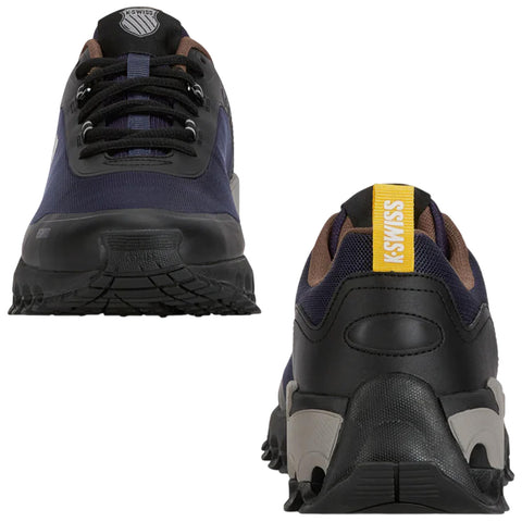 A pair of athletic shoes is positioned upright displaying a navy upper with black and brown accents showcasing laces and a yellow heel tab with the text KSWISS visible.