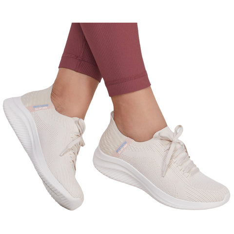 Light beige slip-on sneakers are being worn by a person with their legs partially visible in form-fitting maroon leggings while standing on a neutral background