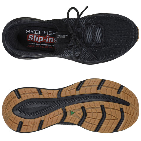 A black Skechers slip-on shoe with a textured fabric upper is displayed. The shoe features a cushioned insole and a rubber outsole with a patterned tread for traction.