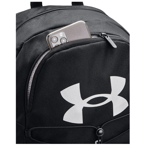 A black backpack with a prominent white logo has a smartphone partially inserted into its front pocket showcasing the bag's storage capacity and practical design for carrying personal items.