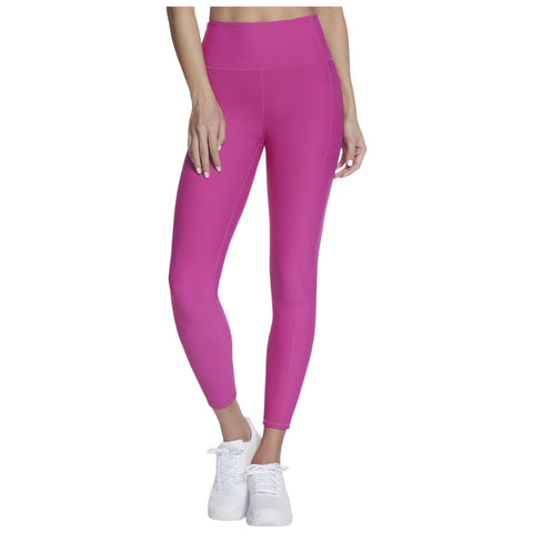 Fitted pink leggings are worn by a person who stands with one hand on their hip and the other by their side in a neutral setting likely indoors, paired with white sneakers.