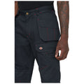 Dark cargo pants with red stitching feature multiple pockets and a branded patch on the thigh while a hand grips the waistband in a neutral background.