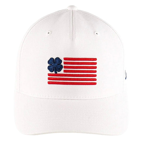 A white baseball cap features an embroidered design of a stylized American flag with red stripes and a blue four-leaf clover emblem positioned to the left of the flag.