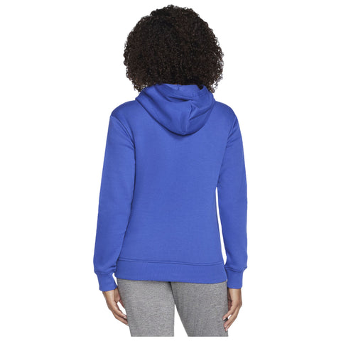 A person wearing a blue hoodie is standing with their back to the viewer. The person has curly black hair and is dressed in gray pants in a neutral setting.