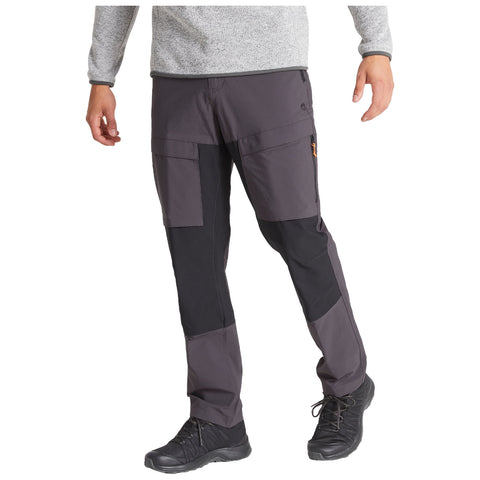 Dark gray hiking pants with multiple pockets are being worn by a person standing in a casual pose in a neutral setting. The pants feature contrasting black panels and are paired with black footwear.