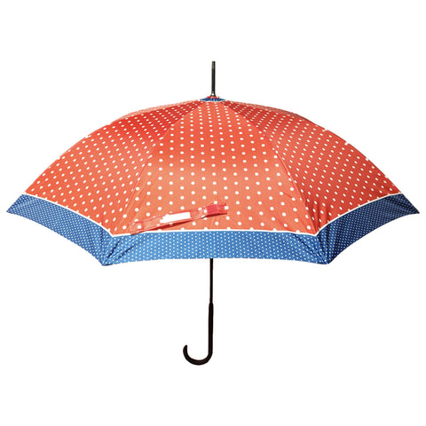 A polka-dot umbrella is opened with a red canopy featuring white dots and a blue trim. It is prominently displayed against a neutral background.