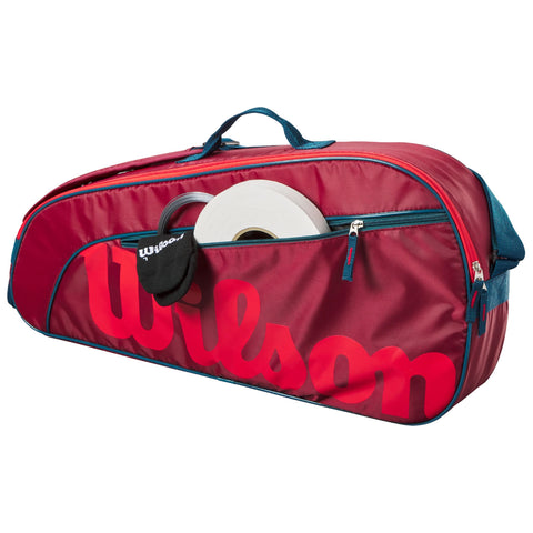 A red tennis bag with a large Wilson logo is open revealing a white roll and a black sock inside it while resting on a flat surface.