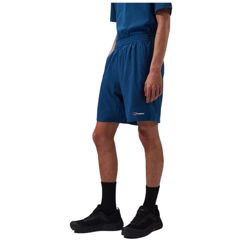 A person stands confidently wearing a blue shirt and matching shorts with black socks and shoes in a neutral setting focused on casual athletic attire.