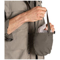 A person holds a small khaki bag containing a light-colored item while wearing a grey jacket showing its zip and pockets against a white background.