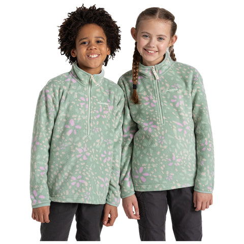 Two children stand side by side smiling wearing matching light green fleece pullovers with pink floral patterns in a neutral background.