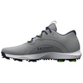 A gray athletic shoe is positioned sideways featuring a smooth upper and a textured sole with green spikes designed for traction in outdoor sports environments.