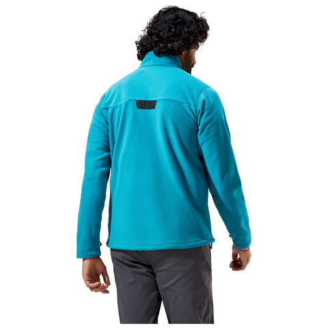 A man wearing a bright turquoise fleece jacket stands with his back to the viewer in a neutral setting showcasing the garment's style and texture.