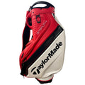 Taylormade Tour Staff Bag V9765701 A golf bag in red and white features the TaylorMade logo prominently. It stands upright with a handle at the top and zippers visible for storing golf clubs and accessories.