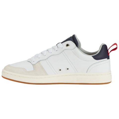 A white sneaker with a gum sole features a mix of leather and suede materials The design includes a navy blue heel and a red pull tab on the back