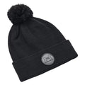 A black knit beanie is resting on a flat surface with a pom-pom on top and a branded patch featuring the logo of Under Armour on the cuff