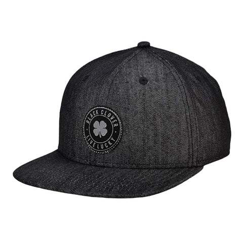 A black baseball cap with a flat brim features a circular logo on the front that includes a four-leaf clover and the text Live Lucky and Black Clover