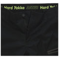 Black pants are displayed with a visible zipper and button closure featuring a waistband that has the text "ACTIVE Hard Yakka" in bright green writing along the top edge.